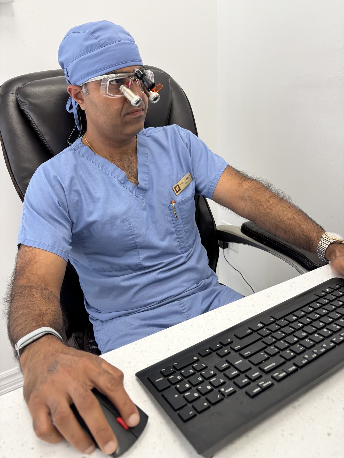 Dr. Vijay Singh in scrubs and dental loupes at his desk