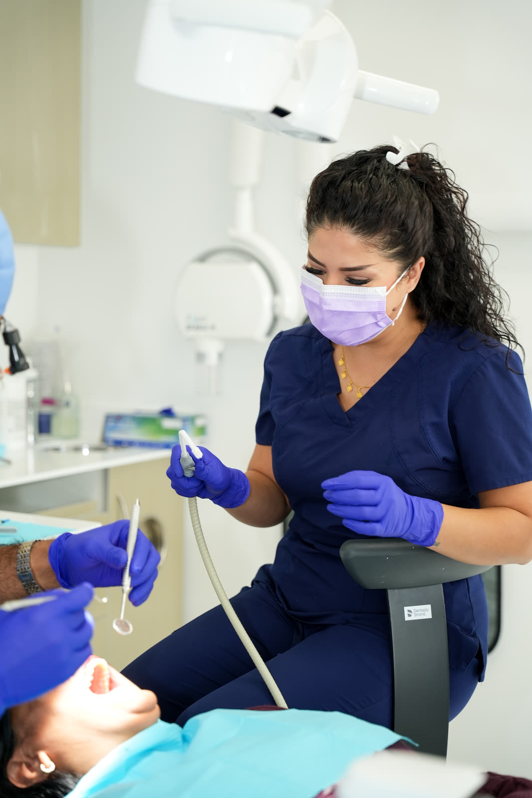 Shakila in a mask and gloves assisting at the dental chair