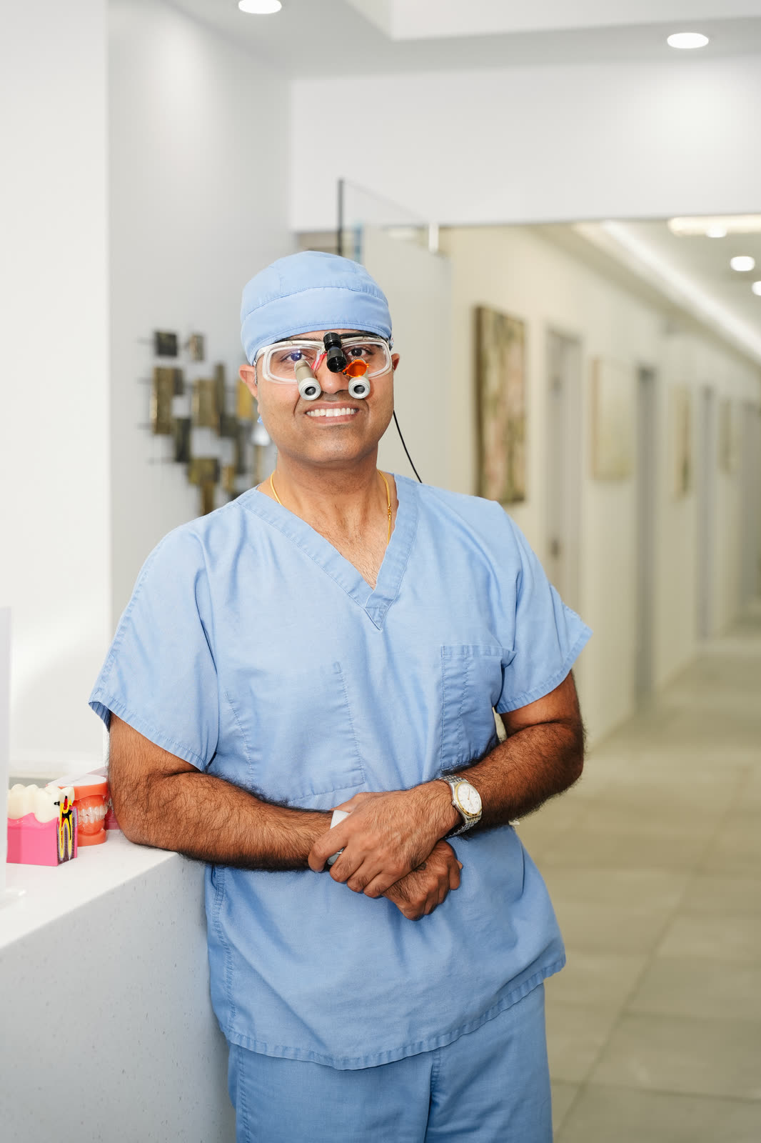 Dr. Vijay Singh in scrubs and dental loupes in the hallway