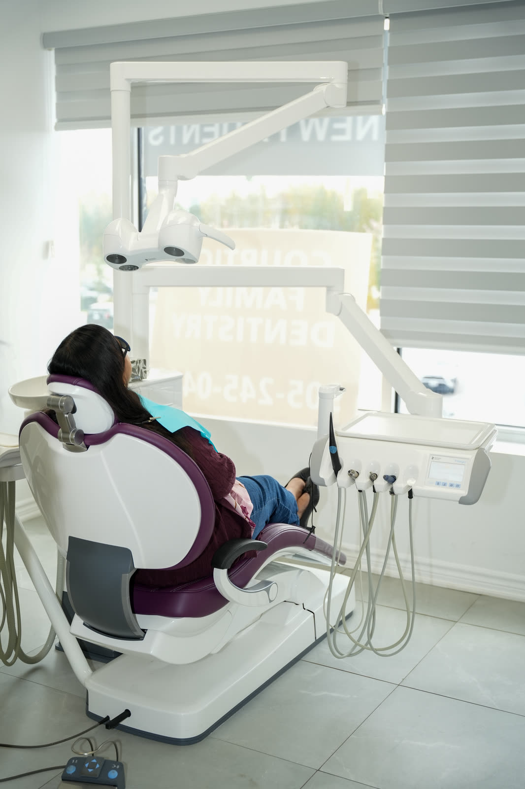 A patient in a dental chair beside a window with blinds