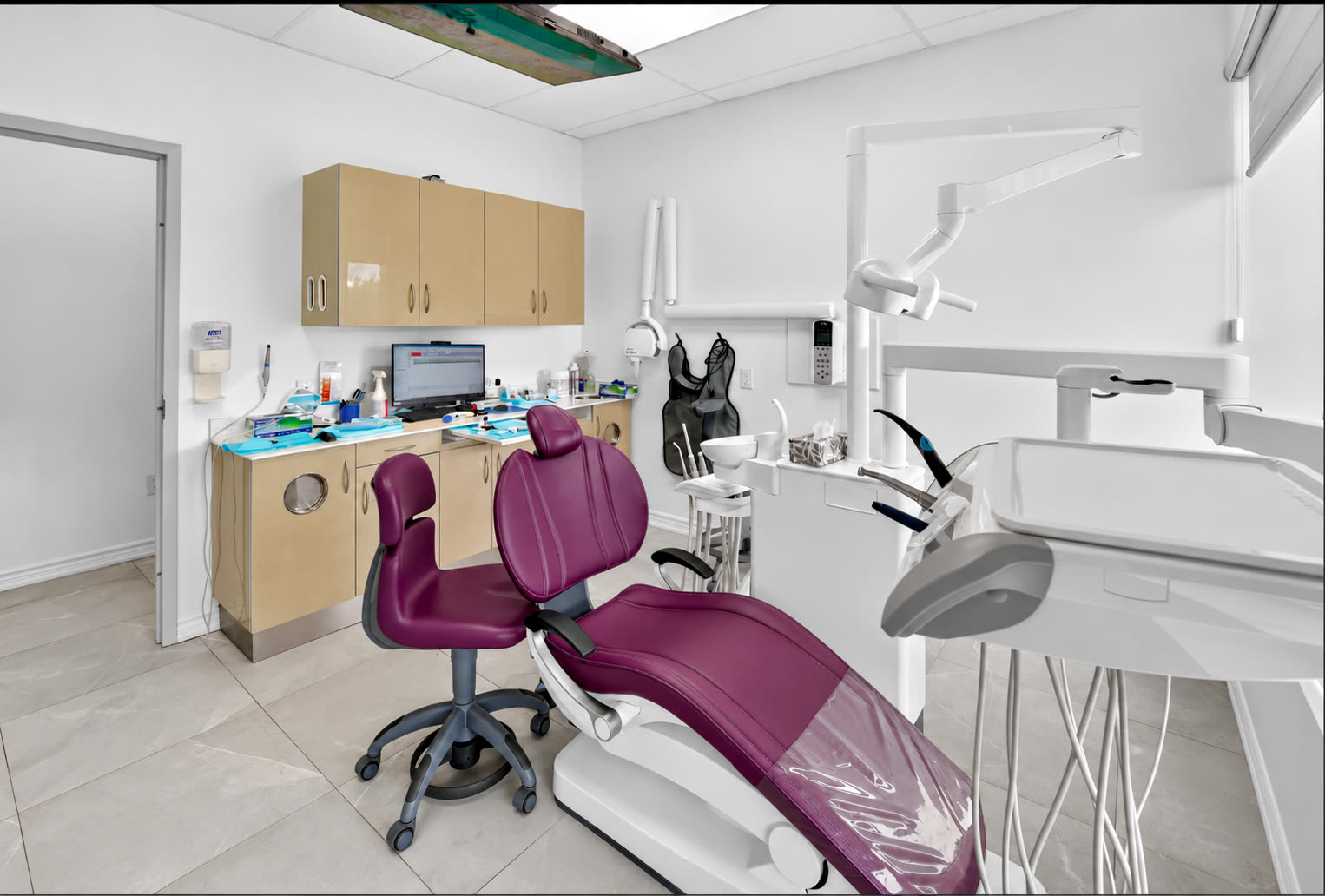 Treatment room with a plum dental chair and wood cabinets