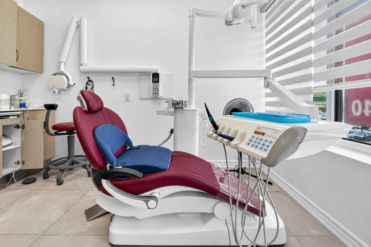Treatment room with a red dental chair beside the window