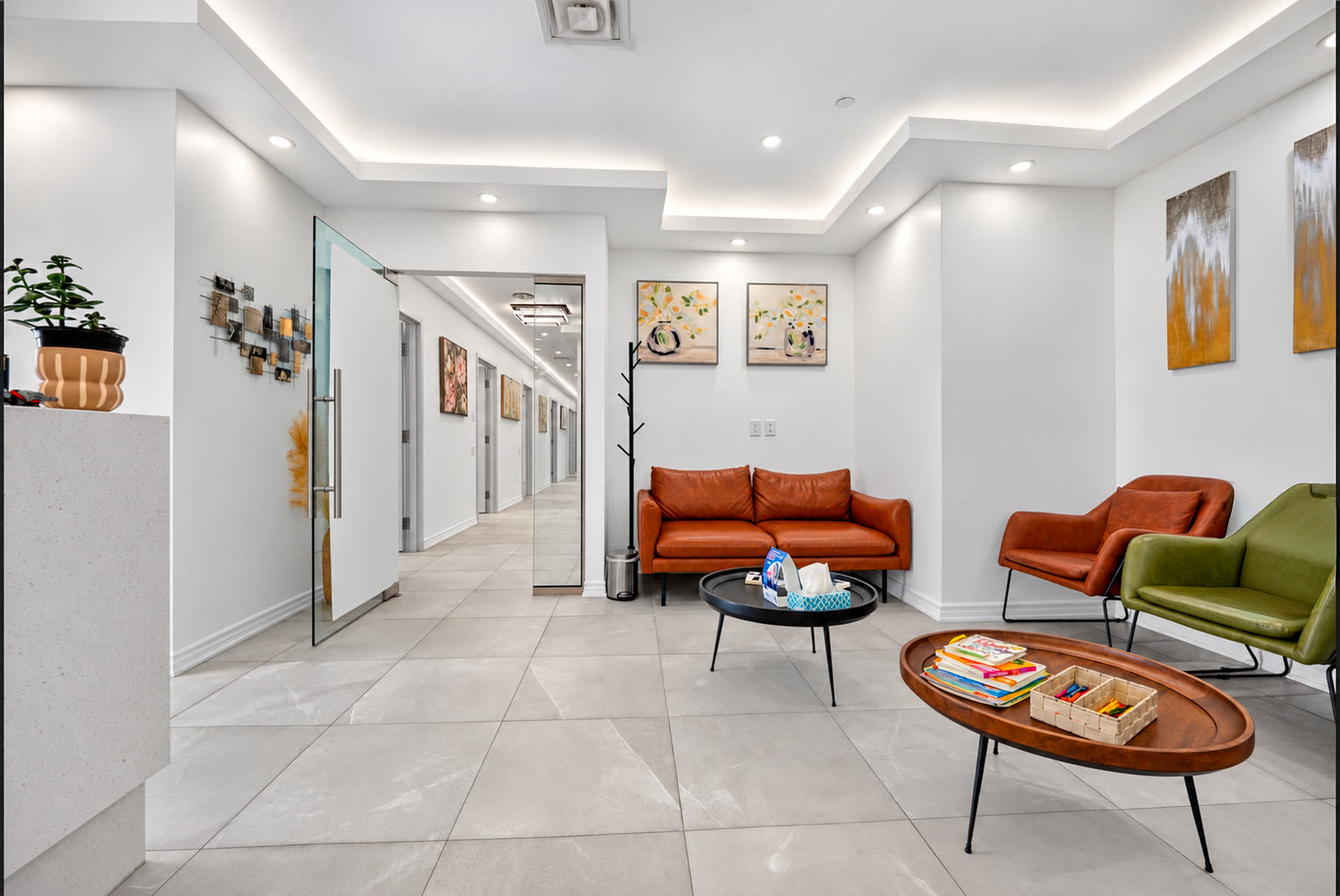 Waiting room with orange and green armchairs, coffee tables and the hallway to the treatment rooms